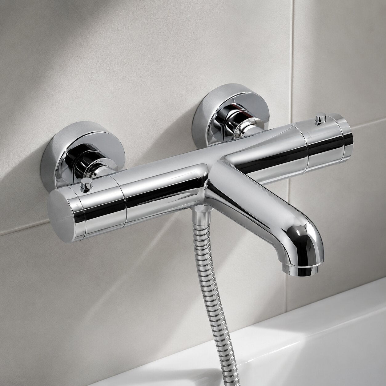 Modern chrome exposed thermostatic bath shower mixer tap with integrated bath filler spout, thermostatic temperature control, flexible shower hose and ceramic wall tiles in a contemporary UK bathroom.