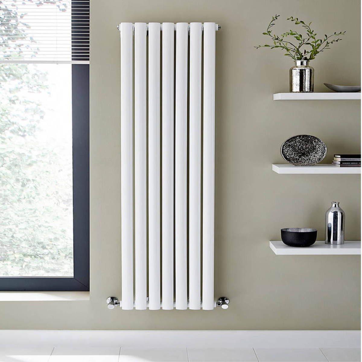 White vertical radiator on a wall with a window and shelves in the background