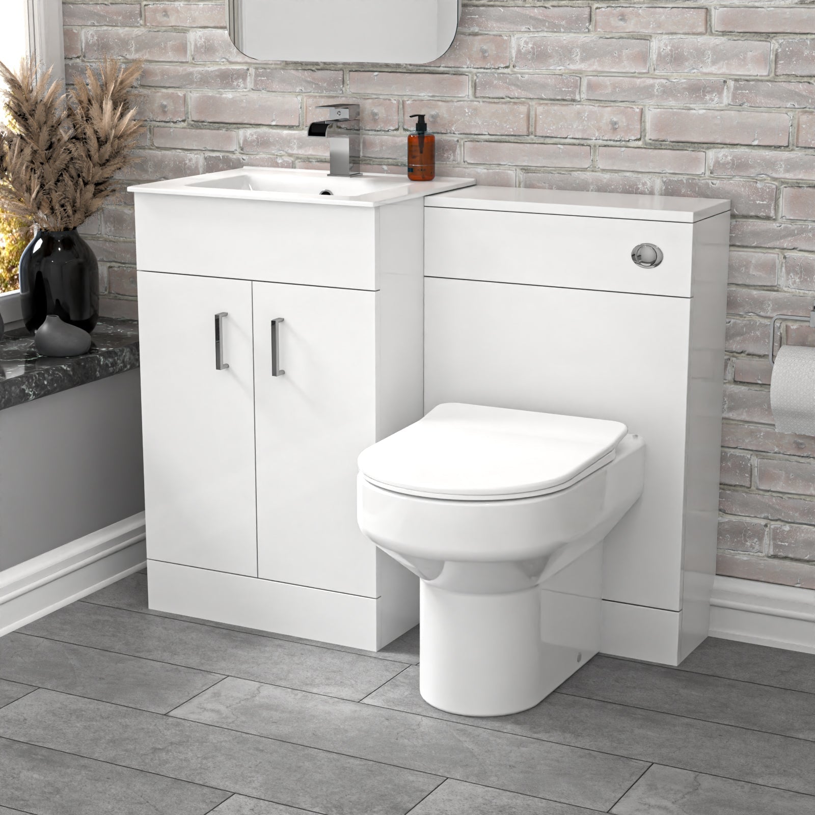 Bathroom setup with white vanity unit, toilet, and sink against a brick wall.