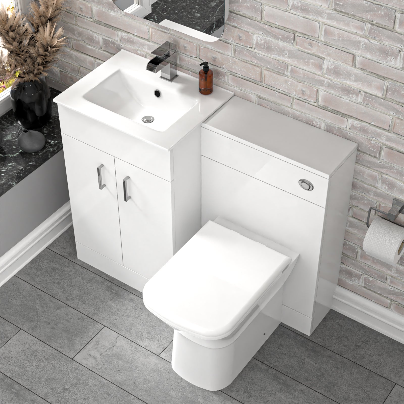 Bathroom setup with white vanity unit, sink, and toilet and faucet against a brick wall.