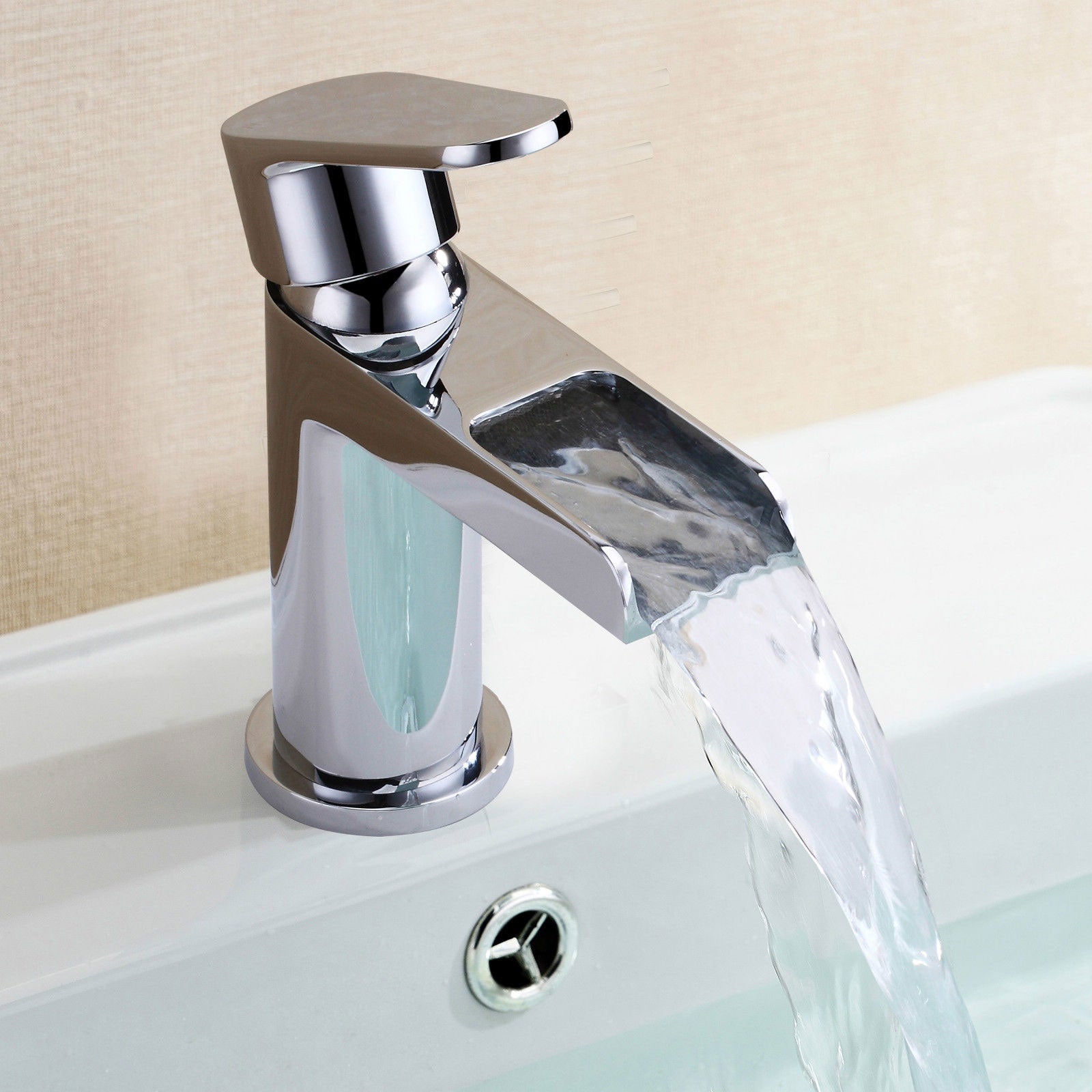 Chrome faucet with water flowing into a sink against a beige wall.