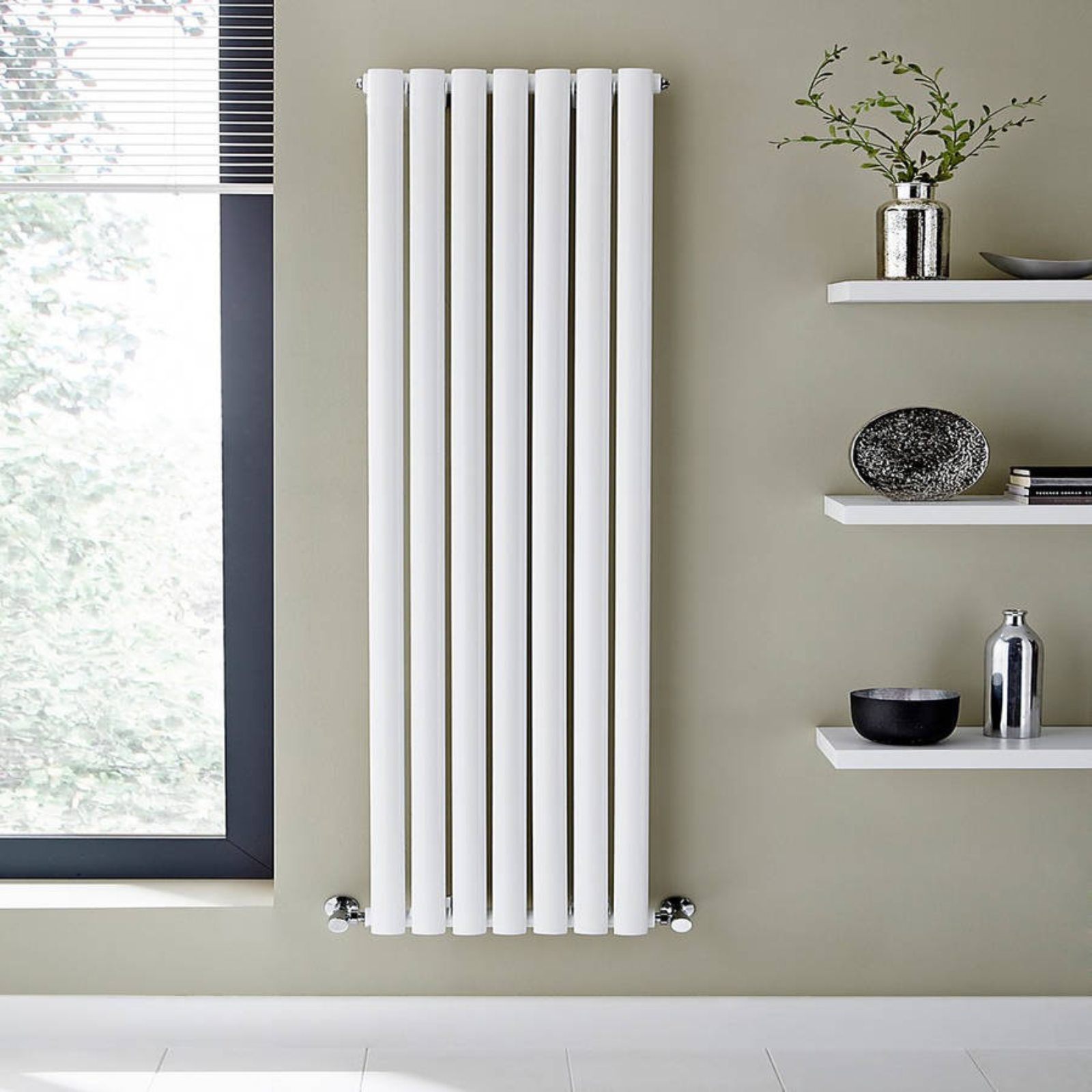 White vertical radiator against a wall with shelves holding decorative items.