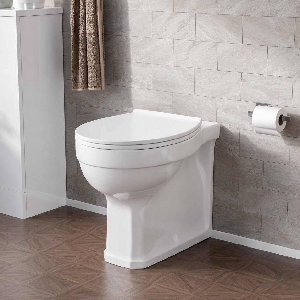 Modern white close coupled toilet with soft close seat installed in a contemporary UK bathroom featuring stone-effect wall tiles and wood-effect flooring.
