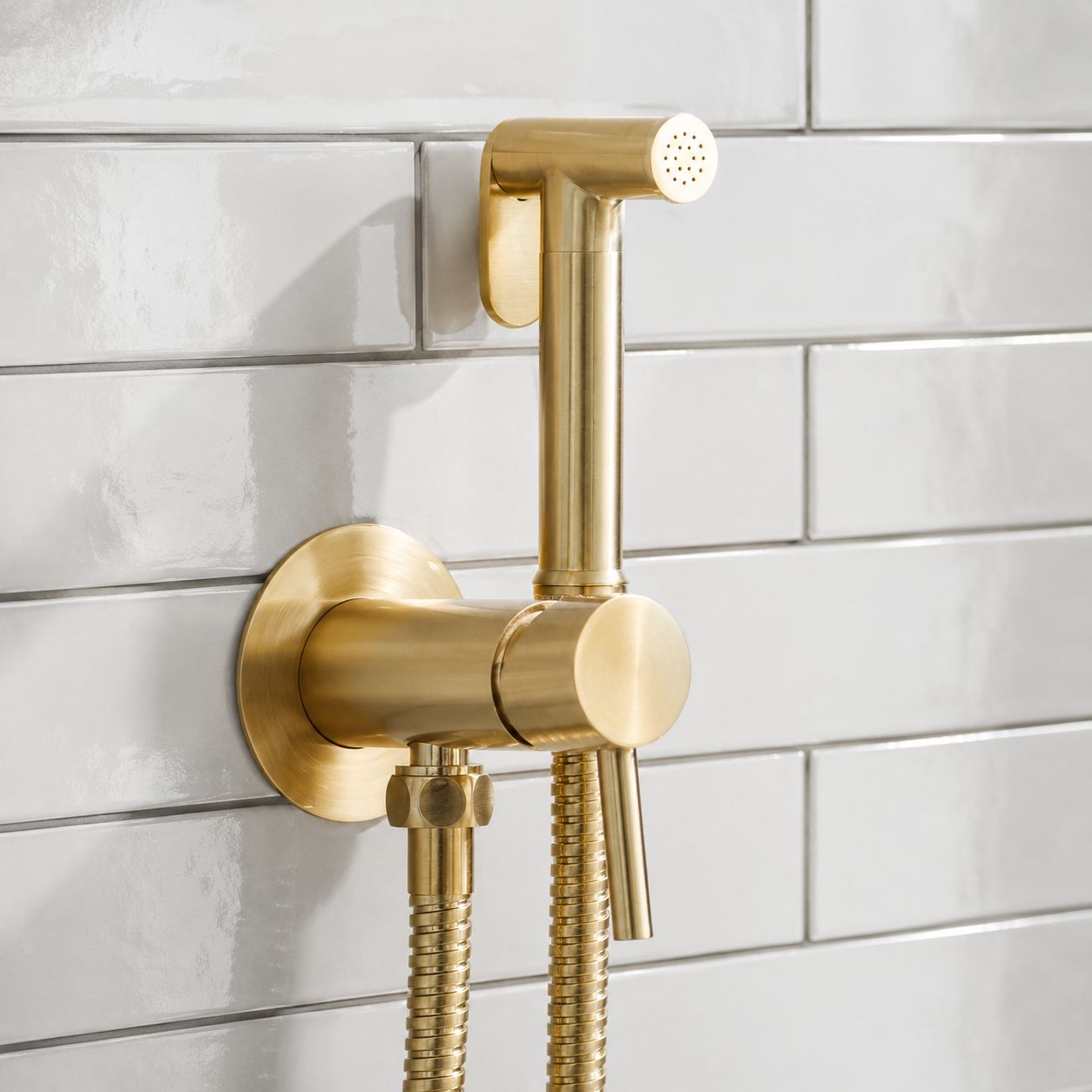 Brushed brass hand-held bidet douche spray with flexible hose mounted on a dark tiled bathroom wall — Bathroom Republic UK