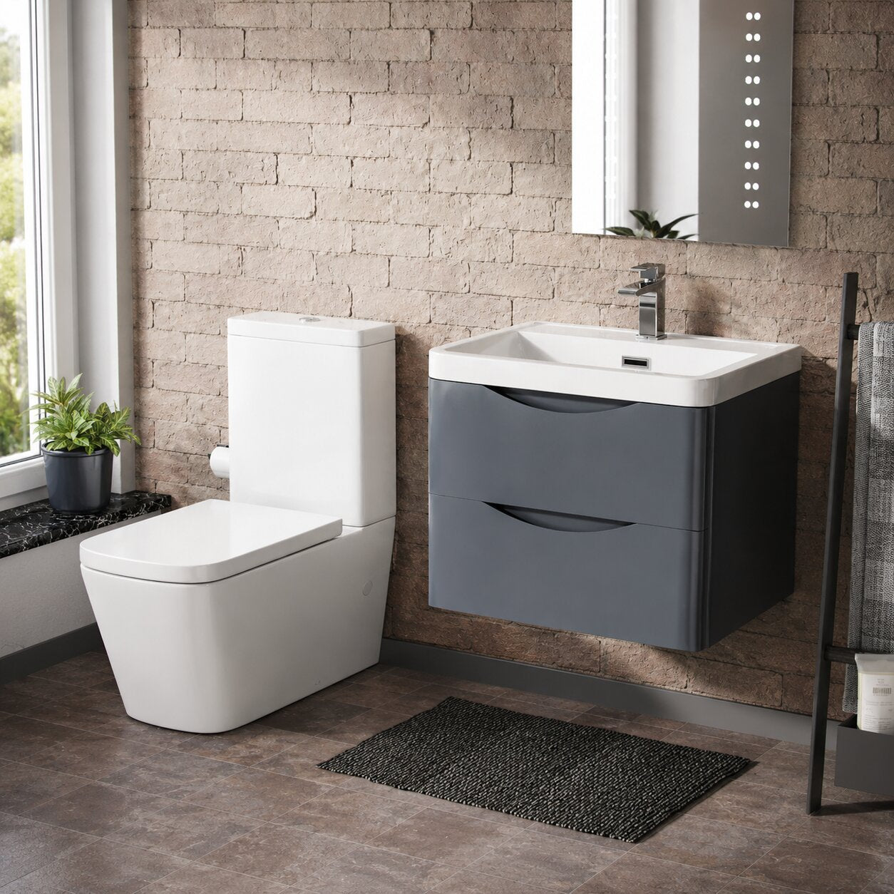 Modern floating grey vanity unit with white ceramic basin, close coupled toilet and LED bathroom mirror in a contemporary UK bathroom with textured brick wall.