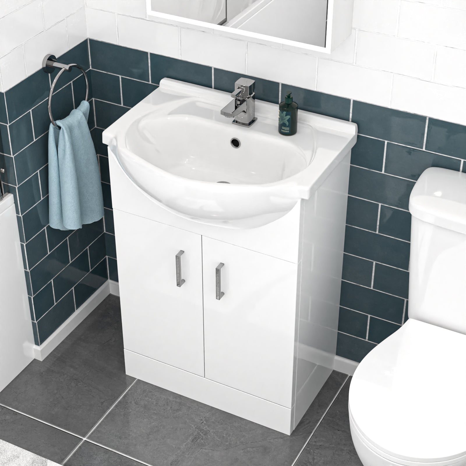 Bathroom setup with a white vanity unit, sink, and toilet against a tiled wall.