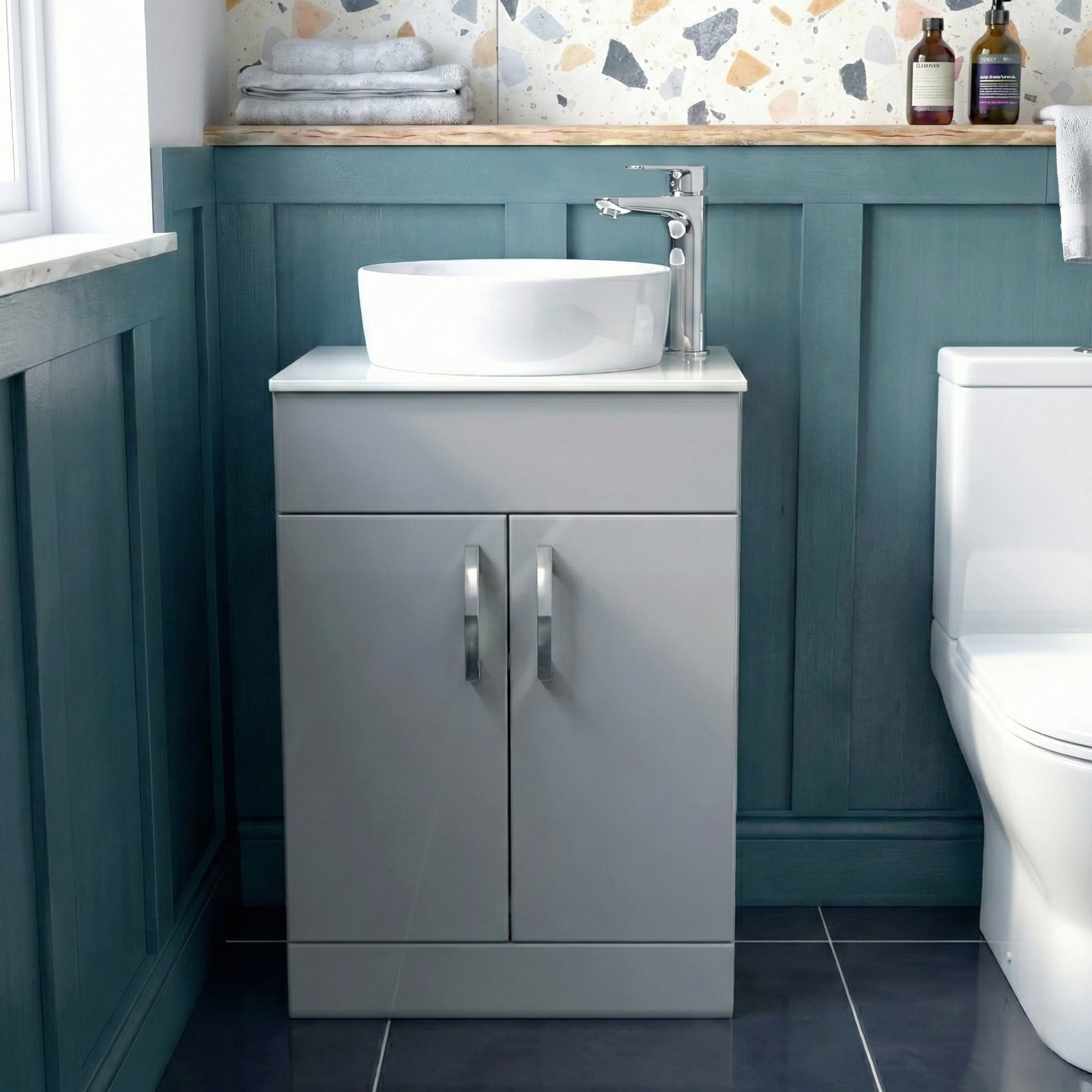 Bathroom with a gray vanity unit, white sink, and toilet against a teal wall.