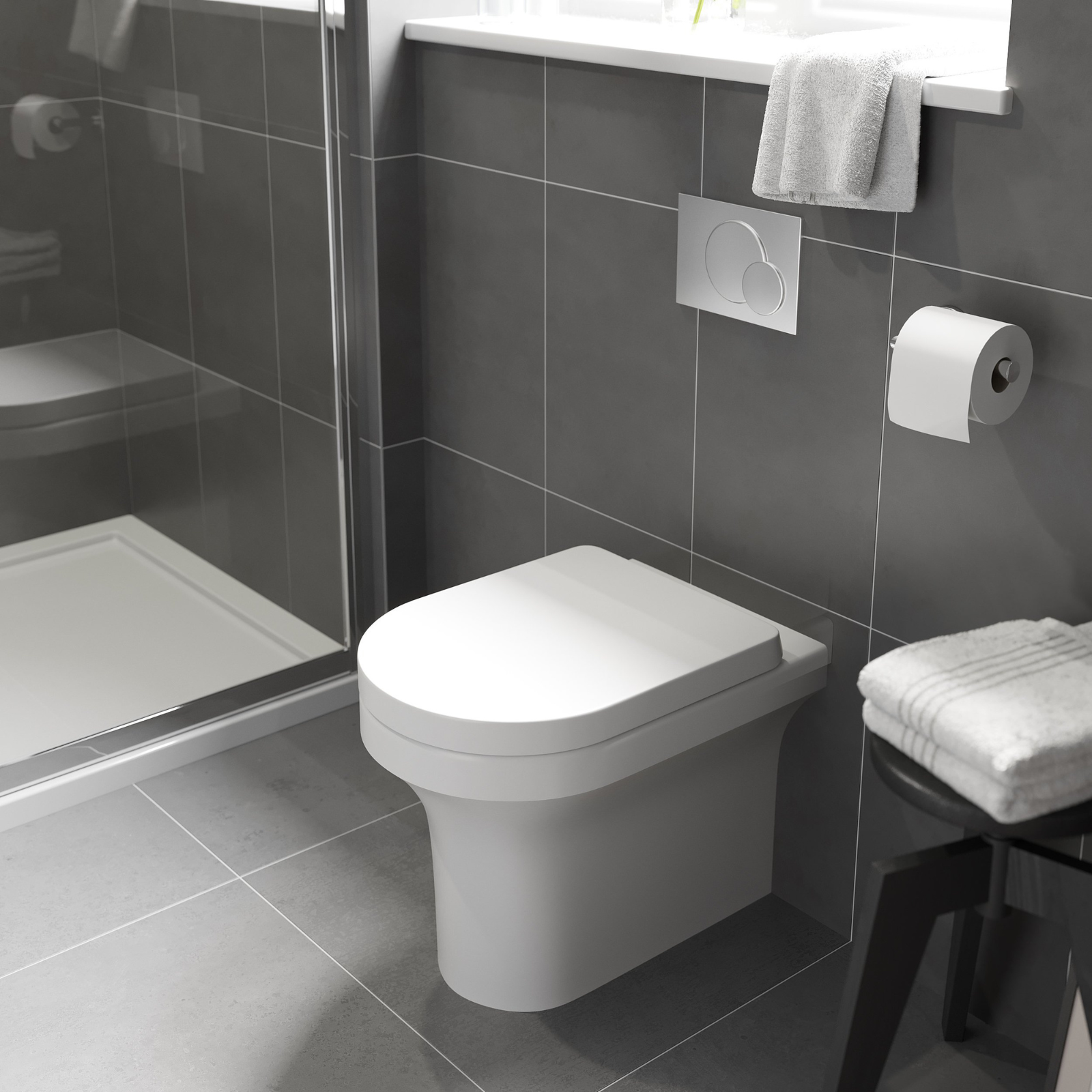 Bathroom with a toilet, towel, and toilet paper on gray tiled walls.