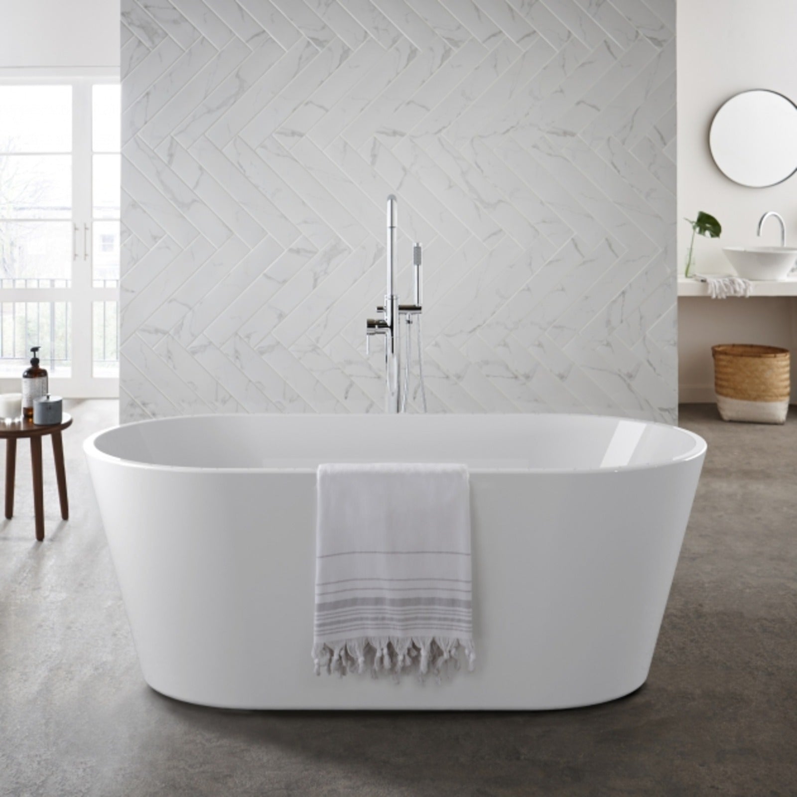 White freestanding bathtub in a modern bathroom with marble walls and a wooden stool.