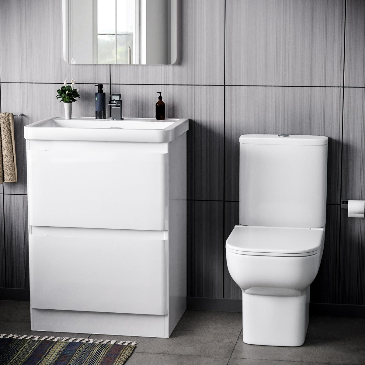 Bathroom setup with a white vanity unit and toilet against a tiled wall.
