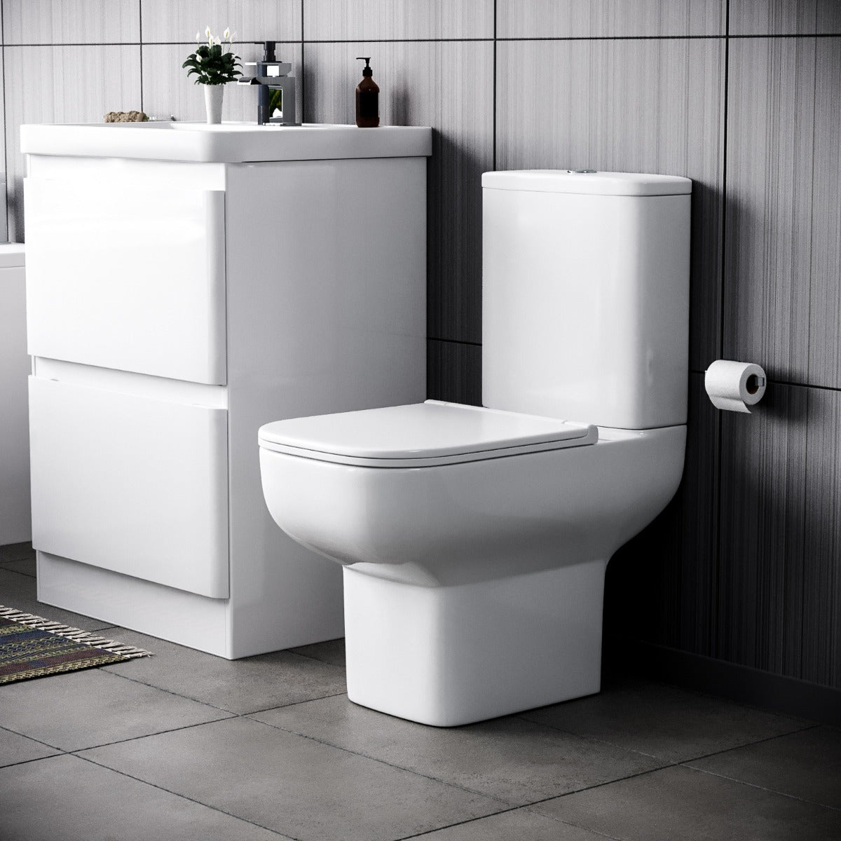 Bathroom setup with a white toilet and vanity unit against a tiled wall.