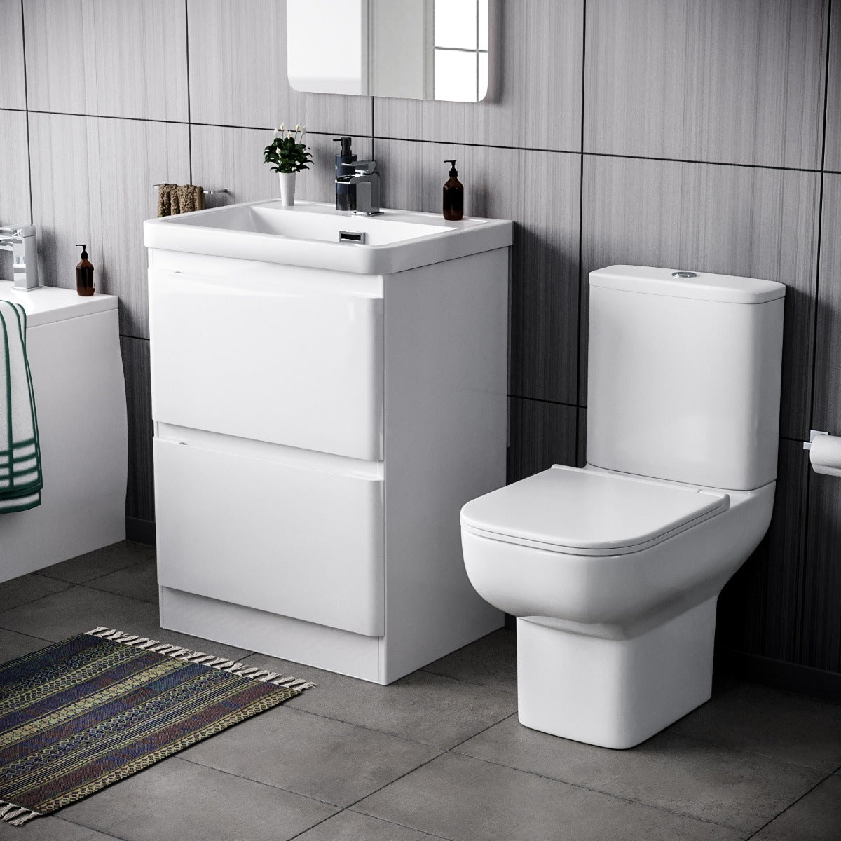 Bathroom setup with a white vanity unit and toilet against a tiled wall.