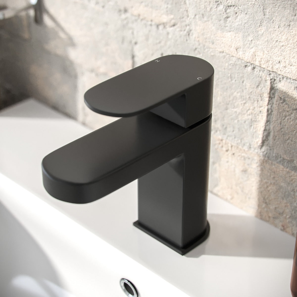 Black faucet on a bathroom sink with a stone wall background